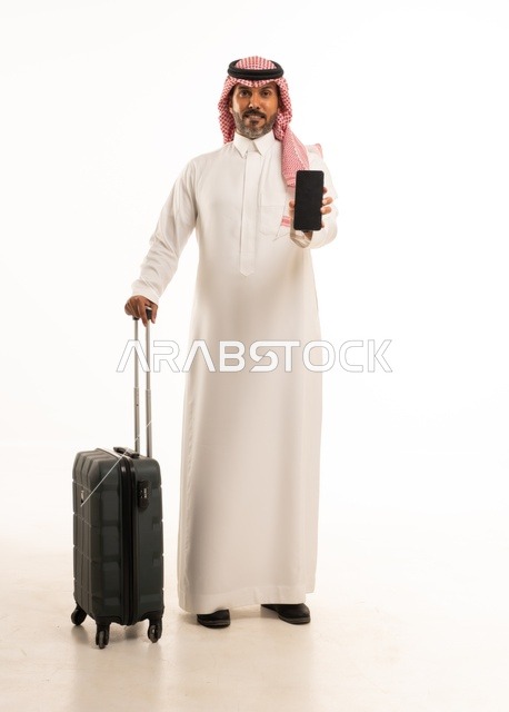 The use of modern and advanced devices, preparing for travel and enjoyable trips, a portrait of a Saudi Arabian Gulf man wearing traditional attire and a headscarf, holding a travel bag and a mobile phone, a full-body image, white background.