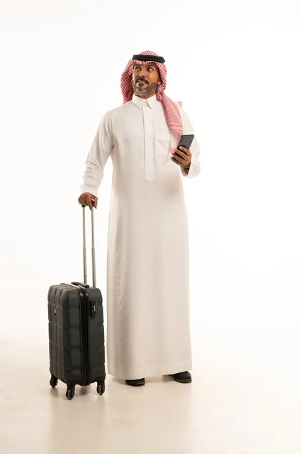 The use of modern and advanced devices, preparing for travel and enjoyable trips, a portrait of a Saudi Arabian Gulf man wearing traditional attire and a headscarf, holding a travel bag and a mobile phone, a full-body image, white background.