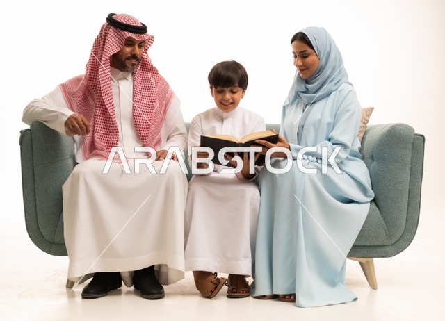 Reading beneficial stories for children, focusing on educating and supporting children, educational activities and developing skills, a portrait of an Arab Gulf couple from Saudi Arabia wearing traditional attire sitting on a sofa teaching their son, utilizing free time by engaging in the hobby of reading, white background.