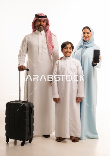 عرض شاشة سوداء فارغة عبر الهاتف، تجهيز حقيبة السفر، أنشطة سياحية ترفيهية، التأهب لرحلة سفر و قضاء اوقات ممتعة في العطلة، بورتريه لزوجان عربيان خليجيان سعوديان يقفان مع ابنهما بإيماءات السعادة والسرور، المحافظة على تماسك الأسرة، الجسم بالطول الكامل، خلفية بيضاء