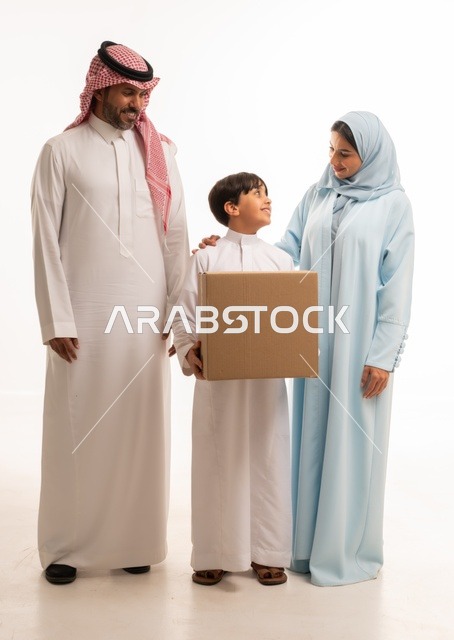 Cooperation and sharing in moving boxes of household items, a portrait of a Saudi Gulf Arab family standing in their new home looking at the camera with gestures of happiness and joy at owning a new residence, a boy holding a cardboard box, arranging and organizing the home, the concept of housing, ownership, and family stability, white background.