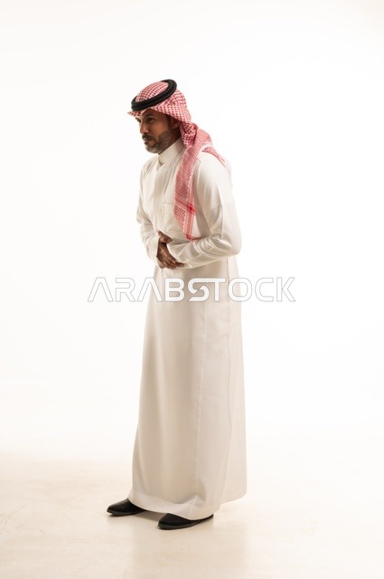 تعابير يد على البطن وجود خطبا ما، الاهتمام بالمظهر الخارجي والأناقة، تعابيرالألم والمعاناة، بورتريه لرجل عربي خليجي سعودي يرتدي الثوب التقليدي، شاب سعودي ،مفهوم التعبير بالإشارة، صورة الجسم بالطول الكامل، خلفية بيضاء