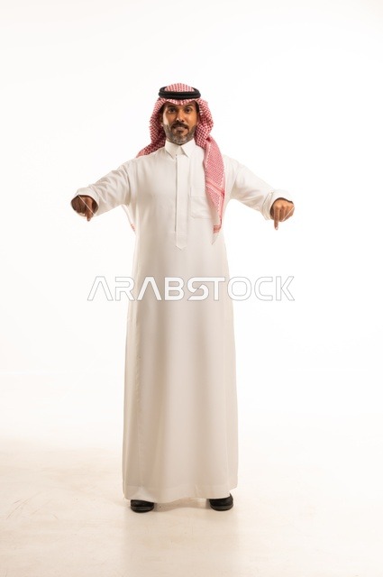 أشارة يدين الأصبعين متجهتين نحو الأسفل ، الاهتمام بالمظهر الخارجي والأناقة، تعابير سرور وابتسامة ، بورتريه لرجل عربي خليجي سعودي يرتدي الثوب التقليدي، شاب سعودي ،مفهوم التعبير بالإشارة، صورة الجسم بالطول الكامل، خلفية بيضاء