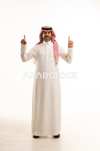 أشارة يدين الأصبعين متجهتين نحو الأعلى ، الاهتمام بالمظهر الخارجي والأناقة، تعابير سرور وابتسامة ، بورتريه لرجل عربي خليجي سعودي يرتدي الثوب التقليدي، شاب سعودي ،مفهوم التعبير بالإشارة، صورة الجسم بالطول الكامل، خلفية بيضاء