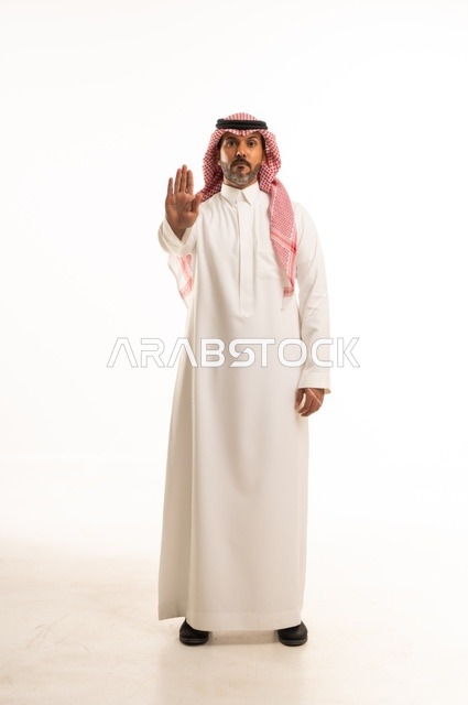 أشارة يد قف لا تكمل تعابير وجه صارمة، الاهتمام بالمظهر الخارجي والأناقة، تعابير جدية وحزم  ، بورتريه لرجل عربي خليجي سعودي يرتدي الثوب التقليدي، شاب سعودي ،مفهوم التعبير بالإشارة، صورة الجسم بالطول الكامل، خلفية بيضاء