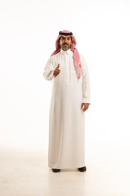 أشارة باستخدام اصبع الأبهام للأعلى تعابير وجه ابتسامة، الاهتمام بالمظهر الخارجي والأناقة، تعابير السرور والسعادة، بورتريه لرجل عربي خليجي سعودي يرتدي الثوب التقليدي، شاب سعودي ،مفهوم التعبير بالإشارة، صورة الجسم بالطول الكامل، خلفية بيضاء