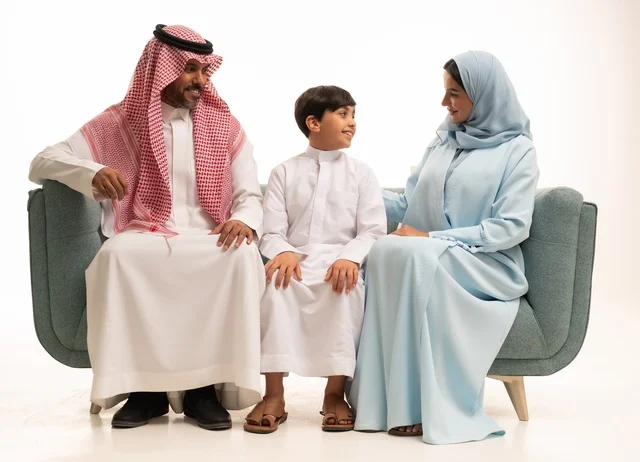 قضاء أوقات عائليه سعيده وممتعه في أيام العطله، نقاشات وحوارات الأباء مع الأبناء، بورتريه لأسره عربيه خليجيه سعودية تجلس على الاريكة وتتبادل أطراف الأحاديث، مفهوم العائله السعوديه المترابطه، بناء علاقات أسريه قويه، خلفية بيضاء.