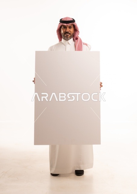 لوحات توضيحية ووسائل تعليمية, العروض والإعلانات التسويقية, بورتريه لرجل عربي خليجي سعودي يرتدي الثوب الأبيض التقليدي يمسك بيديه لوحة بيضاء مستطيلة فارغة، شاب سعودية ينظر إلى الكاميرا بتعابير الحزم والجدية، موك اب مستطيل أبيض, خلفية بيضاء