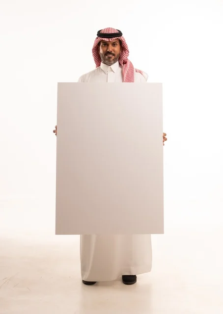 لوحات توضيحية ووسائل تعليمية, العروض والإعلانات التسويقية, بورتريه لرجل عربي خليجي سعودي يرتدي الثوب الأبيض التقليدي يمسك بيديه لوحة بيضاء مستطيلة فارغة، شاب سعودية ينظر إلى الكاميرا بتعابير الحزم والجدية، موك اب مستطيل أبيض, خلفية بيضاء