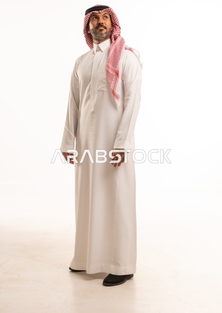 تعابير وجه ابتسامة يدين على الجانب، الاهتمام بالمظهر الخارجي والأناقة، تعابير السرور والسعادة، بورتريه لرجل عربي خليجي سعودي يرتدي الثوب التقليدي، شاب سعودي ،مفهوم التعبير بالإشارة، صورة الجسم بالطول الكامل، خلفية بيضاء