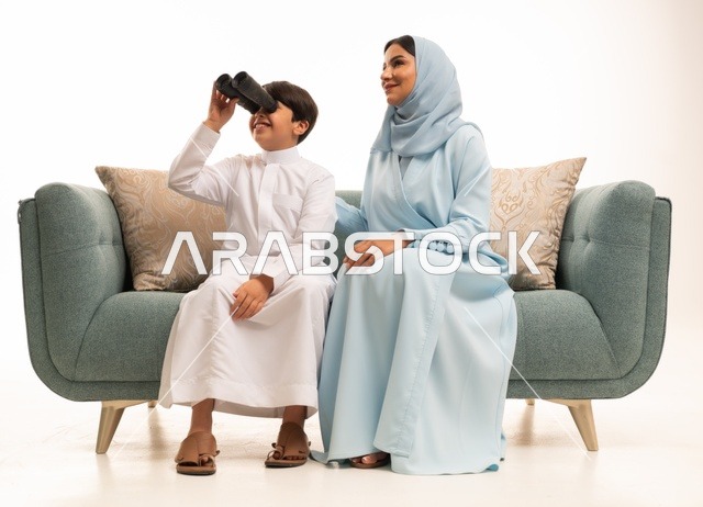 رؤية الأشياء البعيدة، تشجيع الأهل للأبناء على الاستكشاف والمغامرات ،بورتريه لولد عربي خليجي سعودي رفقة والدته يحمل بيده منظار ثنائي العينين يقوم بالتخطيط المستقبلي للأهداف، الاشارة الى شيء ما، الجسم بالطول الكامل، خلفية بيضاء