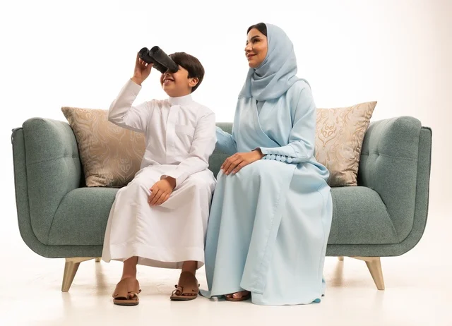 رؤية الأشياء البعيدة، تشجيع الأهل للأبناء على الاستكشاف والمغامرات ،بورتريه لولد عربي خليجي سعودي رفقة والدته يحمل بيده منظار ثنائي العينين يقوم بالتخطيط المستقبلي للأهداف، الاشارة الى شيء ما، الجسم بالطول الكامل، خلفية بيضاء