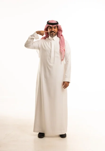 اشارة بالسبابة إلى الوجه تعابير ابتسامة وسرور، الاهتمام بالمظهر الخارجي والأناقة، بورتريه  جانبي لرجل عربي خليجي سعودي يرتدي الثوب التقليدي، شاب سعودي ،مفهوم التعبير بالإشارة، صورة الجسم بالطول الكامل، خلفية بيضاء