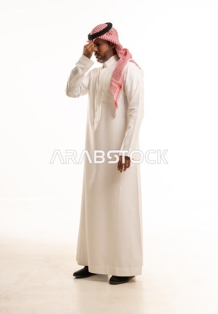 تعابيريد وضع اليد على الأنف ألم في منطقة الجيوب الأنفية، الاهتمام بالمظهر الخارجي والأناقة، بورتريه  جانبي لرجل عربي خليجي سعودي يرتدي الثوب التقليدي، شاب سعودي ،مفهوم التعبير بالإشارة، صورة الجسم بالطول الكامل، خلفية بيضاء