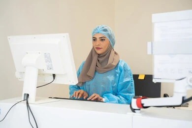 ايماءات التركيز والاندماج، الاستفادة من التصوير الشعاعي والتقنيات الحديثة في مجال طب العيون، استخدام التكنولوجيا المتطورة في التشخيص والعلاج البصري، طبيبة عربية خليجية سعودية ترتدي الزي الرسمي المعقم تتابع صور الأشعة العينية على جهاز الحاسوب داخل المركز الطبي للعيون، فحص دقيق لحالة الشبكية والقرنية، العناية بصحة العين وتحسين الرؤية، خلفية داخلية للمركز الطبي