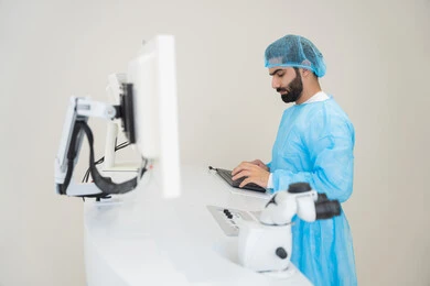 A Saudi Arabian Gulf Arab doctor wearing sterile official attire is reviewing eye radiology images on a computer inside the eye medical center, benefiting from radiographic imaging and modern techniques in the field of ophthalmology, using advanced technology in visual diagnosis and treatment, conducting a thorough examination of the retina and cornea, caring for eye health and improving vision, with an interior background of the medical center.
