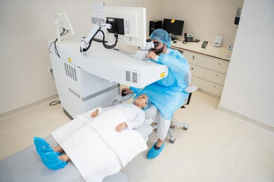 Laser vision correction surgery, eliminating problems of poor vision and nearsightedness, restoring clear vision without the need for glasses, healthy eyes and more accurate vision, a Saudi Arabian Gulf boy wearing sterile official attire sitting in the clinic chair, a Saudi doctor revealing to perform LASIK surgery inside medical centers, focusing on eye care and improving vision.