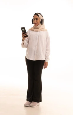 Choosing songs with gestures of joy, listening to favorite music clips, a portrait of a young Arab Gulf Saudi woman wearing a hijab in casual attire, holding a mobile phone in her hands and wearing headphones, using modern headphone technology, full-body image, white background.
