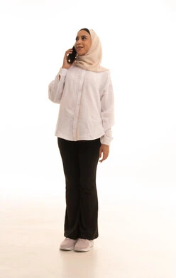 Communicating with family and friends, making a voice call via mobile, integrating modern technologies into daily life, a portrait of a young Arab Gulf Saudi woman wearing a hijab in casual attire holding a mobile phone in her hand, full-body length, white background.