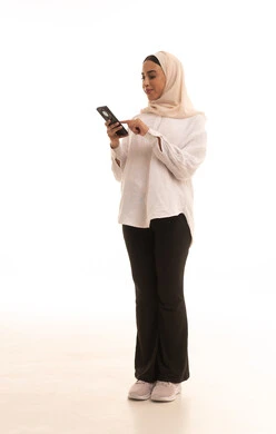 الدردشة مع الأهل والأصدقاء، تصفح مواقع التواصل الاجتماعي، قضاء وقت ممتع عبر الجوال مع الأصحاب، بورتريه لشابة عربيه خليجية سعودية محجبة ترتدي الزي الكاجول تقوم بإرسال الرسائل النصية عبر الهاتف المحمول، الجسم بالطول الكامل، خلفية بيضاء