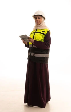 النظر الى الكاميرا بتعابير السرور، اعتماد التقنيات والتكنولوجيا الحديثة في الهندسة،  مهن ووظائف سعودية نسائية، دراسة أساسيات المشروع عبر تطبيقات الجهاز اللوحي, بورترية لمهندسة عربية سعودية خليجية ترتدي سترة وخوذة الحماية تتابع سير أعمال المصنع بإستخدام جهاز التابلت، الجسم بالطول الكامل، خلفية بيضاء