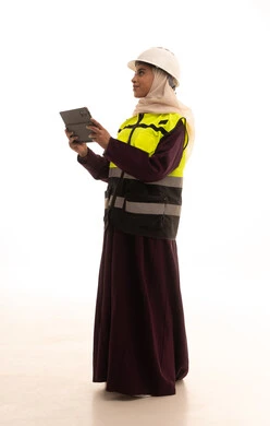 مهن ووظائف سعودية نسائية، دراسة أساسيات المشروع عبر تطبيقات الجهاز اللوحي، اعتماد التقنيات والتكنولوجيا الحديثة في الهندسة, بورترية لمهندسة عربية سعودية خليجية ترتدي سترة وخوذة الحماية تتابع سير أعمال المصنع بإستخدام جهاز التابلت، الجسم بالطول الكامل، خلفية بيضاء