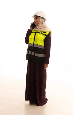 اجراء مكالمه هاتفية عبر الهاتف المحمول، مفهوم الهندسة والانشاءات المعمارية، الإعمار بسواعد أبناء الوطن، استخدام التقنيات والتكنولوجيا الحديثة في القطاع الهندسي، بورتريه لمهندسة عربية خليجية سعودية ترتدي خوذة وسترة الحماية تمسك الهاتف المحمول، الجسم بالطول الكامل، خلفية بيضاء