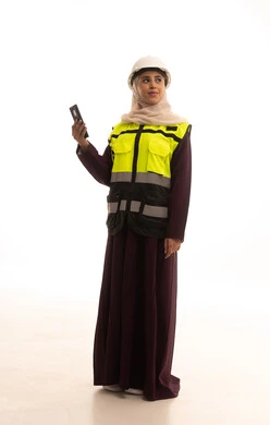 مفهوم الهندسة والانشاءات المعمارية، الإعمار بسواعد أبناء الوطن، استخدام التقنيات والتكنولوجيا الحديثة في القطاع الهندسي، بورتريه لمهندسة عربية خليجية سعودية ترتدي خوذة وسترة الحماية تقوم بتصفح الجوال ، الجسم بالطول الكامل، خلفية بيضاء