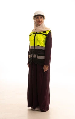 Looking at something, the concept of engineering and architectural construction, working in the engineering sector, standing with gestures of confidence, a portrait of a smiling Arab Gulf Saudi female architect wearing a helmet and safety vest standing upright with crossed arms, a full-body image, white background.