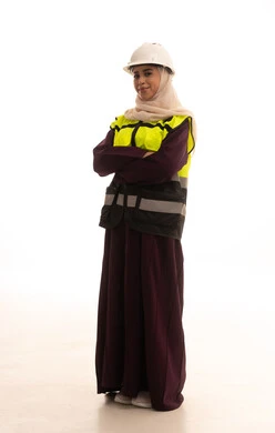 مفهوم الهندسة والإنشاء المعماري، العمل في القطاع الهندسي, الوقوف بايماءات الثقة, بورتريه لمهندسة معمارية عربية خليجية سعودية مبتسمة ترتدي خوذة وسترة الحماية تقف باستقامة وايدي متقاطعه، صورة لكامل الجسم، خلفية بيضاء