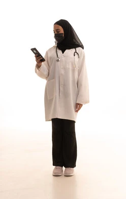 عرض شاشة سوداء فارغة، الحفاظ على السلامة من كوفيد19،  العمل في المراكز والمستشفيات، الطب والرعاية الصحية، بورتريه لطبيبة عربية خليجية سعودية محجبة ترتدي المعطف الطبي الأبيض تضع سماعة الفحص الطبية و الكمامة تحمل بيدها الهاتف المحمول، صورة لكامل الجسم، خلفية بيضاء
