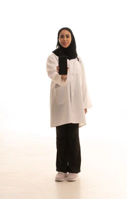 A blank black screen display, working in centers and hospitals, medicine and healthcare, a portrait of a Saudi Arabian Gulf female doctor wearing a white medical coat and holding a mobile phone in her hand, a young Saudi woman providing medical assistance, full-body image, white background.