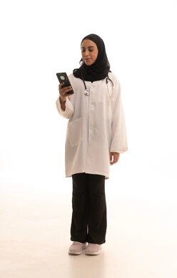 التطبيقات الرقمية للخدمات الصحية, تقديم الخدمات والرعاية الصحية عبر الإنترنت، بورتريه  لطبيبة عربيه خليجيه سعودية ترتدي المعطف الطبي و السماعه تقوم باستخدام الهاتف المحمول، استخدام الأجهزة التقنية الحديثة ودمج التكنولوجيا مع الطب،الجسم بالطول الكامل، خلفية بيضاء