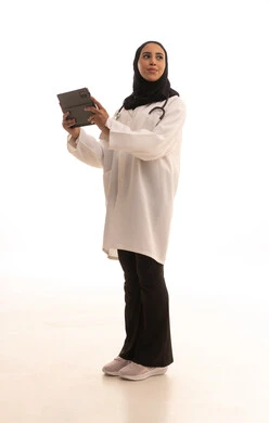 Looking at something, providing remote consultations for patients, technological devices, the development of the healthcare sector in Saudi Arabia, working in the healthcare sector, a portrait of an Arab Gulf Saudi female doctor wearing a white coat and stethoscope holding a tablet device, full-body, white background.