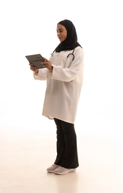 The development of the healthcare sector in the Kingdom of Saudi Arabia, working in the healthcare sector, providing remote consultations for patients using technological devices, a portrait of an Arab Gulf Saudi female doctor wearing a white coat and stethoscope holding a tablet device, full-body, white background.