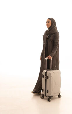 Looking with facial expressions that indicate excitement for a tourist trip, preparing and packing luggage for travel on a tourist tour, the concept of tourism and travel, a side portrait of a smiling Saudi Gulf Arab woman holding a travel bag, full body, white background.