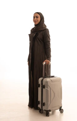 الاستعداد و تجهيز الأمتعة للسفر في جولة سياحية، مفهوم السياحة و السفر، بورتريه من الجانب لامراه عربية خليجيه سعوديه مبتسمه تمسك حقيبة سفر، النظر بايماءات وجه تدل على الحماس للقيام برحلة سياحية، الجسم بالطول الكامل، خلفية بيضاء