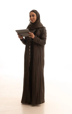 Browsing social media sites and platforms, integrating technology into daily and professional life, a portrait of a Saudi Gulf Arab woman wearing an abaya and hijab using a tablet, the concept of remote project completion, full-body shot, white background.