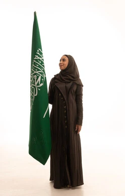 The concept of love for the homeland and belonging to it, Saudi Flag Day on March 11, the celebration of the establishment of the first Saudi state on February 22, the anniversary of the Day of Bidaya in 1727 AD, a portrait of an Arab Gulf Saudi woman wearing an abaya and hijab holding the flag and emblem of the Kingdom, looking with gestures of pride and honor, full-body, white background.
