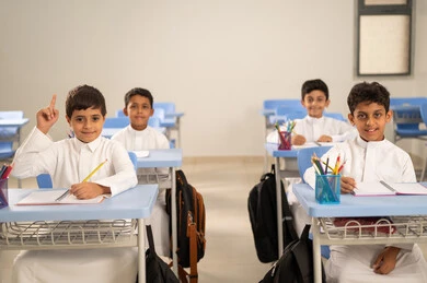 التفاعل والمشاركة داخل الفصل الدراسي، طالب عربي خليجي سعودي مبتسم يرتدي الثوب التقليدي يرفع يديه للإجابة، التربية والتعليم بالمناهج المقررة للطلاب في المملكة العربية السعودية، تعابير وايماءات الحماس لمعرفة الجواب الصحيح