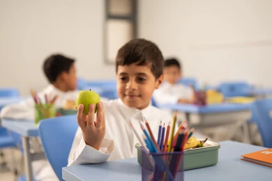 الوجبات الغنية بالعناصر الغذائية الهامة لبناء الجسم،  الاستمتاع بتناول الأطعمة الصحية في وقت الفسحة المدرسية، موسم العودة للمدارس، مجموعة من الطلاب العربيين الخليجيين السعوديين يجلسون في مقاعدهم وأمامهم اللانش البوكسالوجبات الغنية بالعناصر الغذائية الهامة لبناء الجسم