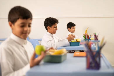 Enjoying healthy food during school break, back-to-school season, a group of Arab Gulf Saudi students sitting in their seats with lunch boxes in front of them, meals rich in essential nutrients for building the body.