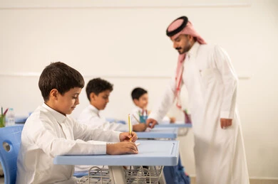 المشاركة الفعالة للطلاب مع المدرسين، مجموعة من طلاب عربيين خليجيين سعوديين يرتدون الزي المدرسي يقومون بتأديه الواجبات ، التربية والتعليم بالمناهج المقررة للتلاميذ، حوارات ودية بين الاستاذ والطلاب،جودة التعليم في السعودية، معلم عربي خليجي سعودي يرتدي الثوب التقليدي والشماغ يقوم بمناقشة الدروس مع طلابه