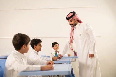 مجموعة من طلاب عربيين خليجيين سعوديين يرتدون الزي المدرسي يقومون بتأديه الواجبات ، المشاركة الفعالة للطلاب مع المدرسين، التربية والتعليم بالمناهج المقررة للتلاميذ،  جودة التعليم في السعودية، معلم عربي خليجي سعودي يرتدي الثوب التقليدي والشماغ يقوم بمناقشة الدروس مع طلابه،حوارات ودية بين الاستاذ والطلاب