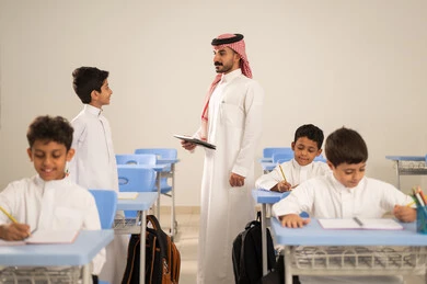 معلم عربي خليجي سعودي يرتدي الثوب التقليدي والشماغ يقوم بمناقشة الدروس مع طلابه يمسك بيده جهاز التابلت ، مجموعة من طلاب عربيين خليجيين سعوديين يرتدون الزي المدرسي يقومون بتأديه الواجبات ، المشاركة الفعالة للطلاب مع المدرسين،حوارات ودية بين الاستاذ والطلاب،استخدام التقنيات الحديثة