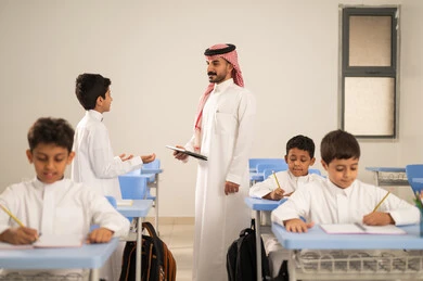 مجموعة من طلاب عربيين خليجيين سعوديين يرتدون الزي المدرسي يقومون بتأديه الواجبات ، المشاركة الفعالة للطلاب مع المدرسين، استخدام التقنيات الحديثة ، معلم عربي خليجي سعودي يرتدي الثوب التقليدي والشماغ يقوم بمناقشة الدروس مع طلابه يمسك بيده جهاز التابلت ، حوارات ودية بين الاستاذ والطلاب