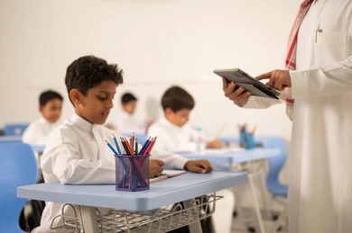 حوارات ودية بين الاستاذ والطلاب، استخدام التقنيات الحديثة ، معلم عربي خليجي سعودي يرتدي الثوب التقليدي والشماغ يقوم بمناقشة الدروس مع طلابه يمسك بيده جهاز التابلت ، مجموعة من طلاب عربيين خليجيين سعوديين يرتدون الزي المدرسي يقومون بتأديه الواجبات ، المشاركة الفعالة للطلاب مع المدرسين،حوارات ودية بين الاستاذ والطلاب
