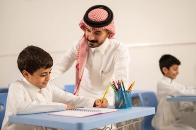 مجموعة من طلاب عربيين خليجيين سعوديين يرتدون الزي المدرسي يقومون بتأديه الواجبات ، المشاركة الفعالة للطلاب مع المدرسين، جودة التعليم في السعودية، معلم عربي خليجي سعودي يرتدي الثوب التقليدي والشماغ يقوم بمناقشة الدروس مع طلابه، التربية والتعليم بالمناهج المقررة للتلاميذ، حوارات ودية بين الاستاذ والطلاب