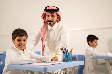 التربية والتعليم بالمناهج المقررة للتلاميذ، جودة التعليم في السعودية، معلم عربي خليجي سعودي يرتدي الثوب التقليدي والشماغ يقوم بمناقشة الدروس مع طلابه، مجموعة من طلاب عربيين خليجيين سعوديين يرتدون الزي المدرسي يقومون بتأديه الواجبات ، المشاركة الفعالة للطلاب مع المدرسين، حوارات ودية بين الاستاذ والطلاب