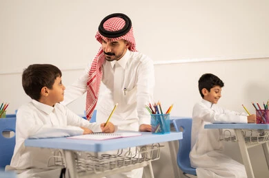 جودة التعليم في السعودية، معلم عربي خليجي سعودي يرتدي الثوب التقليدي والشماغ يقوم بمناقشة الدروس مع طلابه، مجموعة من طلاب عربيين خليجيين سعوديين يرتدون الزي المدرسي يقومون بتأديه الواجبات ، المشاركة الفعالة للطلاب مع المدرسين، التربية والتعليم بالمناهج المقررة للتلاميذ، حوارات ودية بين الاستاذ والطلاب